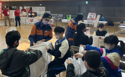 総合防災訓練にて、参加者に三角巾を使った手当の方法を教える女性消防班の様子。